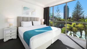 Habitación de hotel con una cama grande, dos mesitas de noche, un buró, una ventana con vistas a la ciudad y un cuadro en la pared.