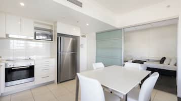 A modern kitchen with white cabinets, a stainless steel refrigerator, a microwave, and an oven. There is a dining area with a white table and chairs.