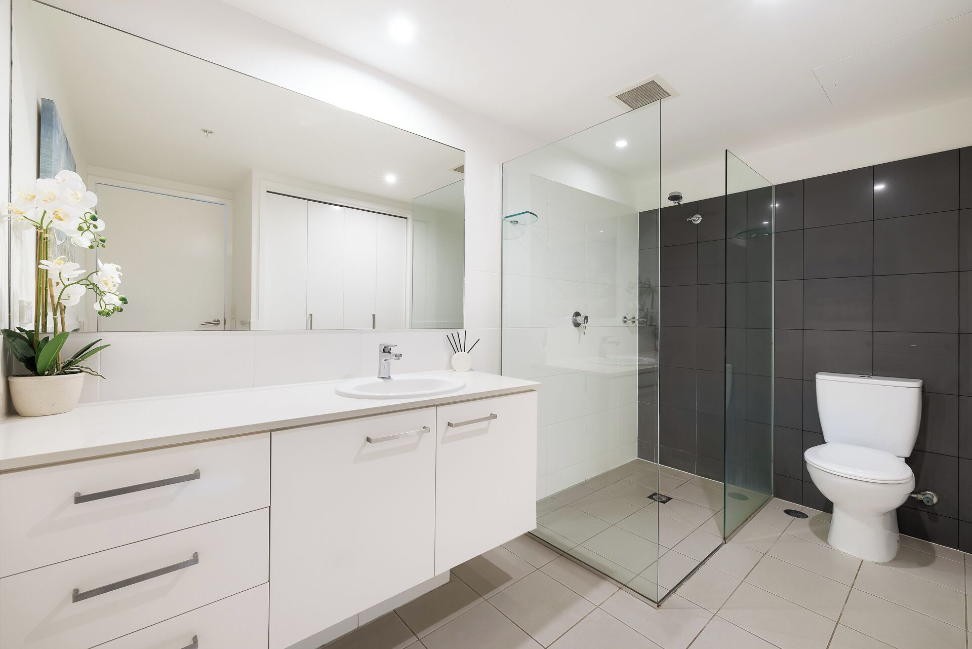 A modern bathroom with a white vanity, a glass shower enclosure, and a white toilet.