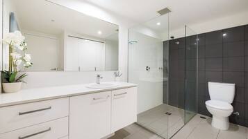 A modern bathroom with a white vanity, a glass shower enclosure, and a white toilet.