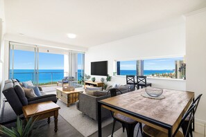 A spacious living area with a balcony overlooking the sea, a dining table, and comfortable seating. - Ocean Pacific Broadbeach (Broadbeach)