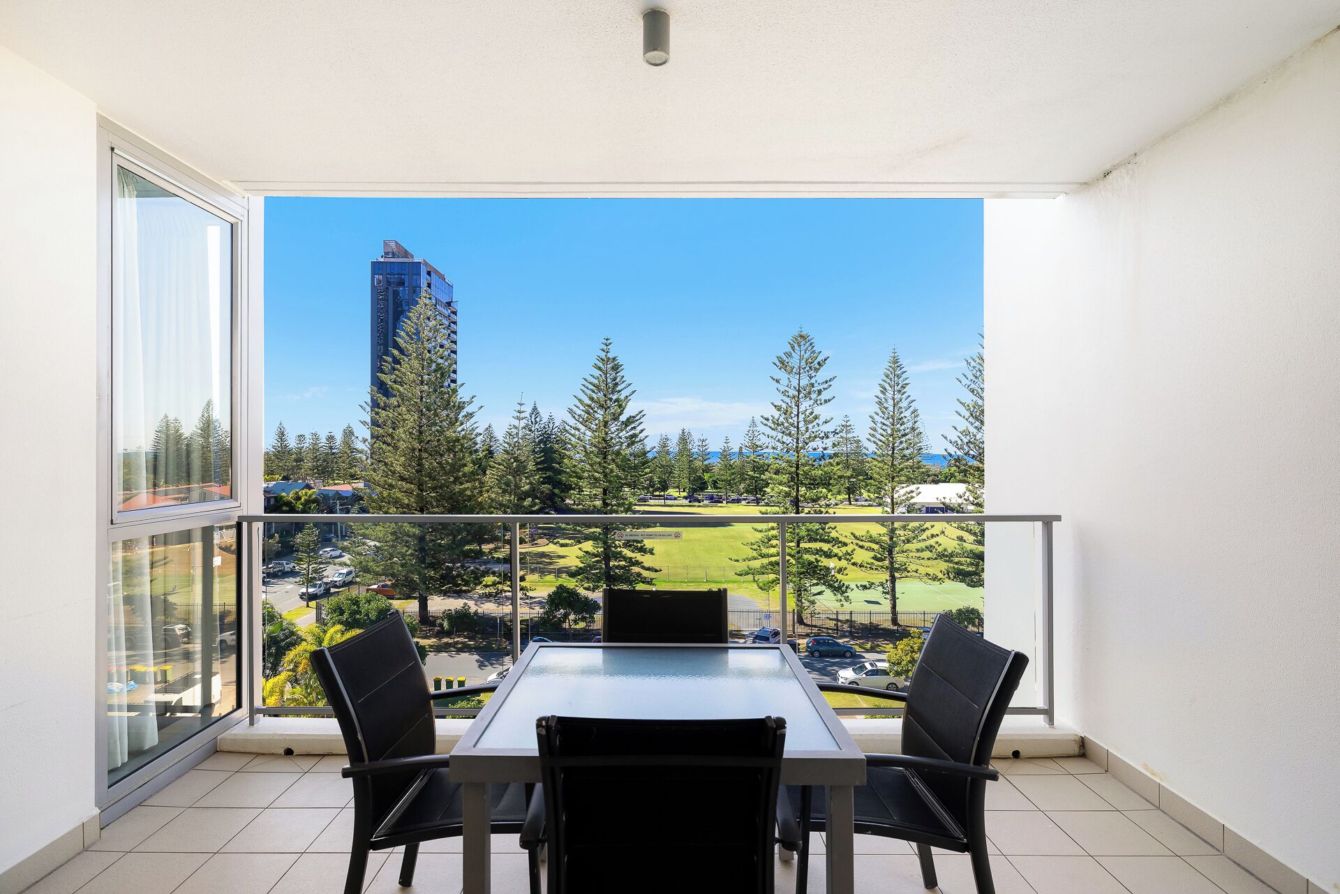 A balcony with a table and chairs, overlooking a cityscape with tall buildings and a park.