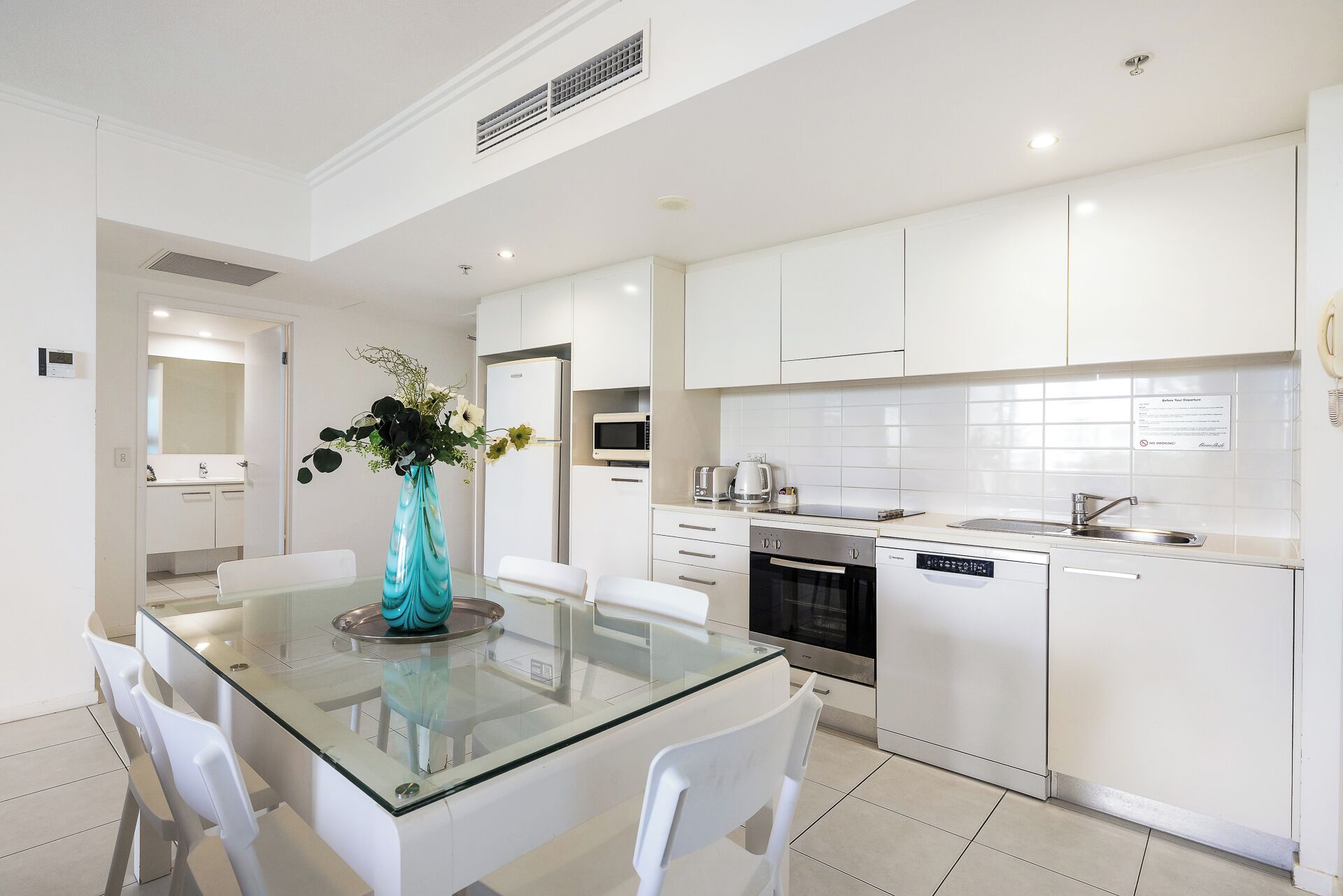 A modern kitchen with white cabinetry, a glass dining table, and white chairs.