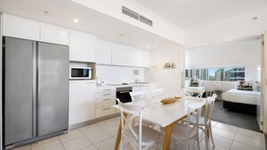 Una cocina moderna con armarios blancos, un refrigerador de acero inoxidable y un comedor con sillas y una mesa blancos.