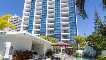 A modern hotel with a large pool area, outdoor seating, and a view of a tall building.