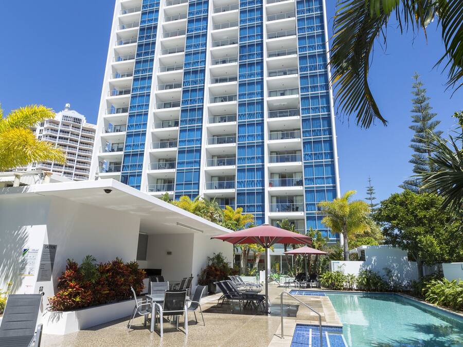 Un hotel moderno con un amplio área de piscina, mobiliario exterior y vistas a un edificio alto.