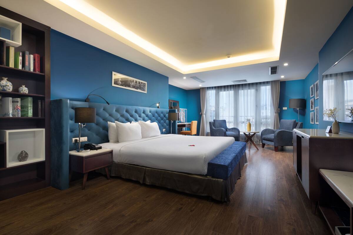 A modern hotel room with a large bed, a desk, and a seating area.
