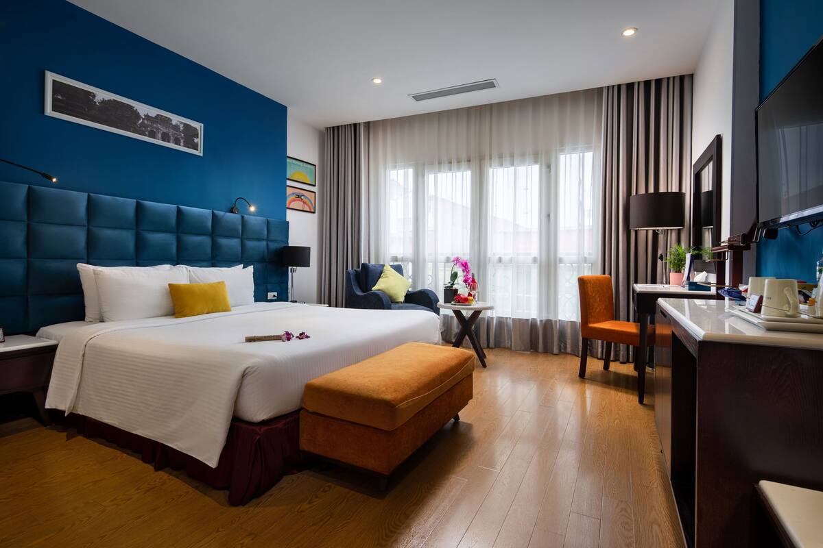 A hotel room with a large bed, a desk, a chair, and a TV.
