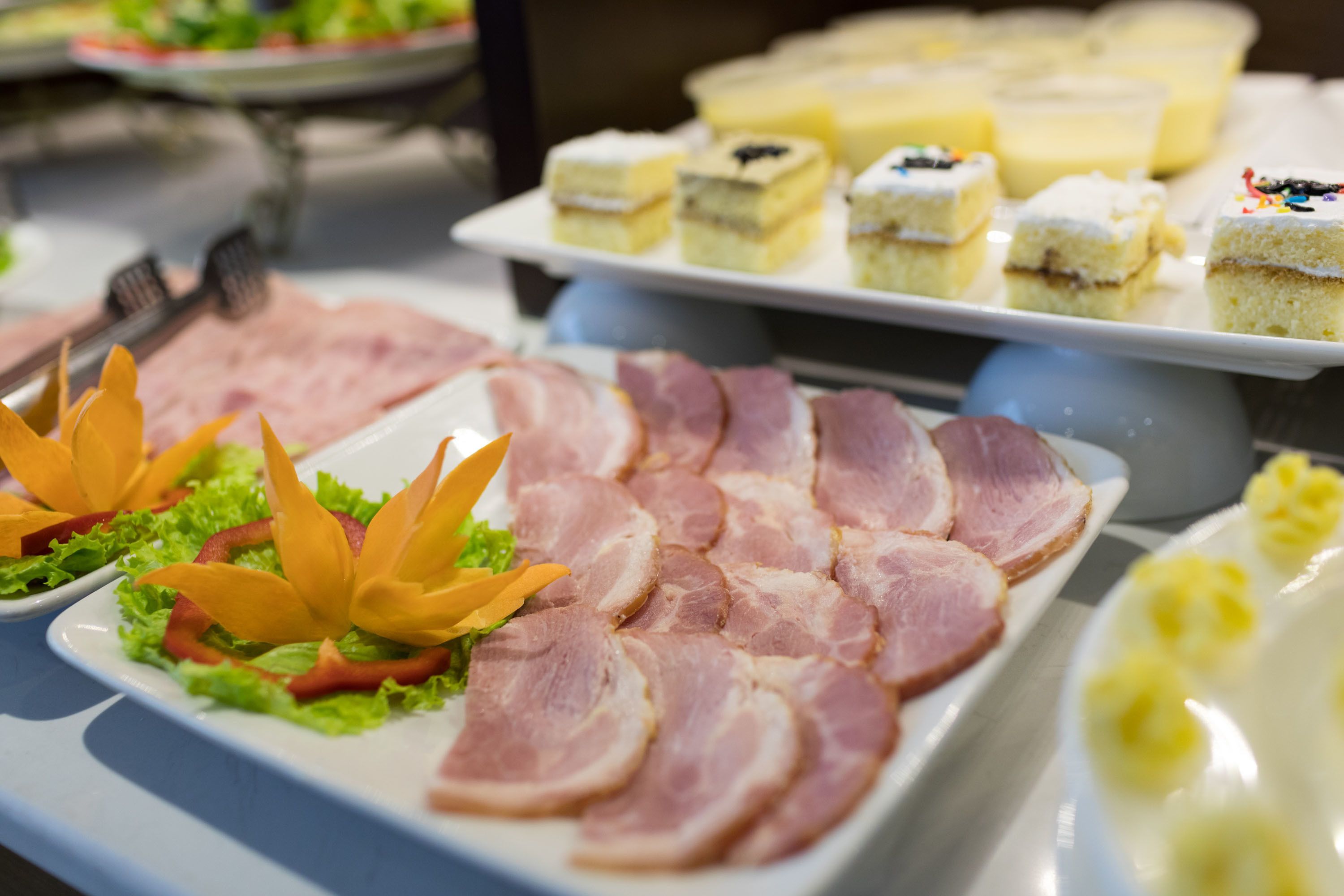A buffet with various food items including ham, cakes, and a decorative arrangement of vegetables.