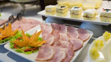 A buffet with various food items including ham, cakes, and a decorative arrangement of vegetables.