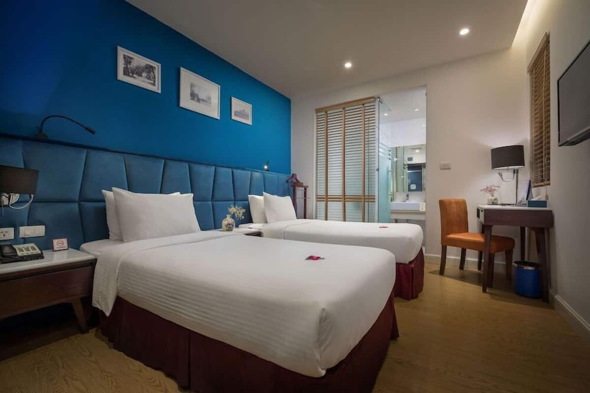 Een hotelkamer met twee bedden, een bureau, een stoel en een badkamer zichtbaar door een schuifdeur.
