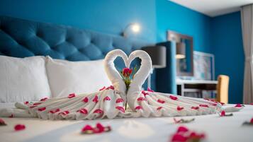 Un lit bien fait, agrémenté d’une décoration en forme de cœur réalisée avec des serviettes et de pétales de rose, le tout mis en valeur par un mur bleu.