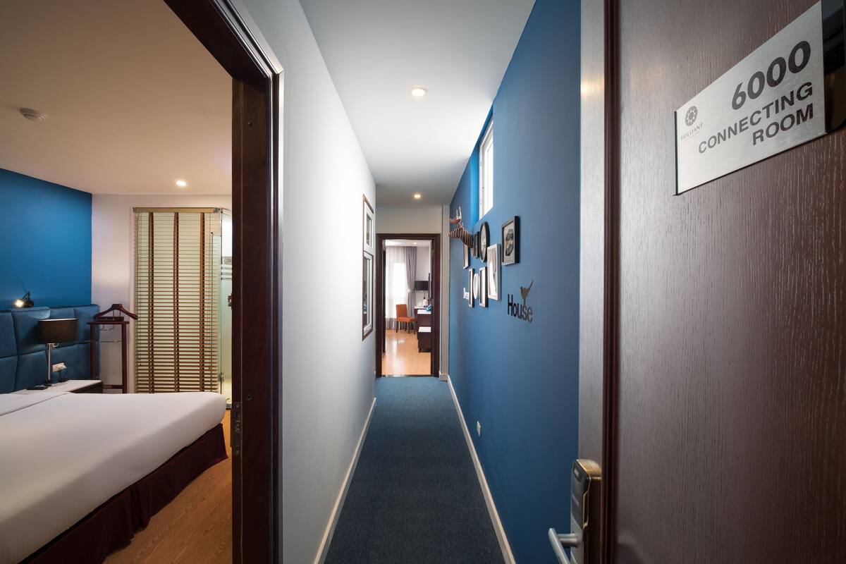 A hotel hallway with a blue carpet, a bed on the left, and a sign indicating room 6000.