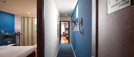 A hotel hallway with a blue carpet, a bed on the left, and a sign indicating a connecting room.