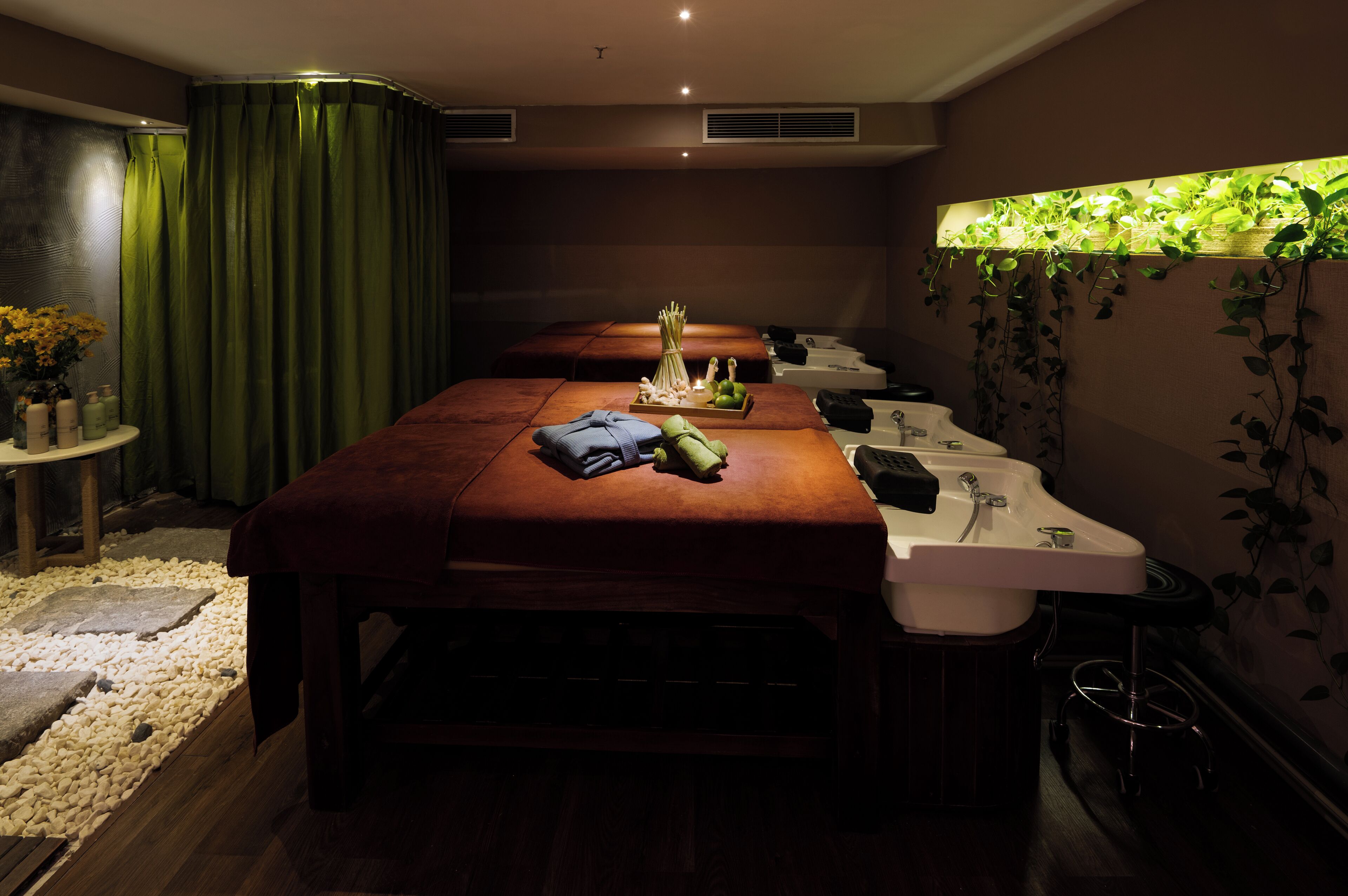 Una stanza spa con un lettino da massaggio, due lavabi, un tavolino con articoli da toilette e una tenda verde.