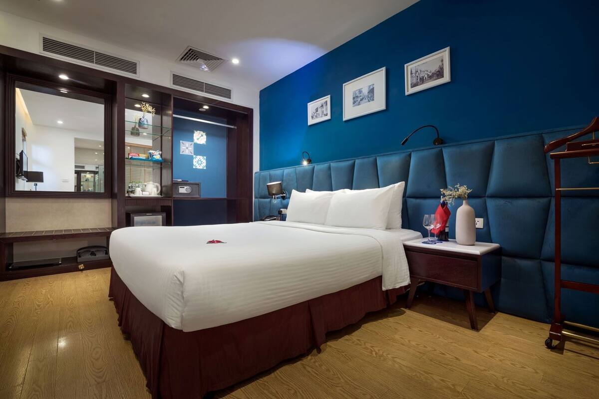A hotel room with a large bed, a nightstand, a mirror, a blue accent wall, and framed pictures.