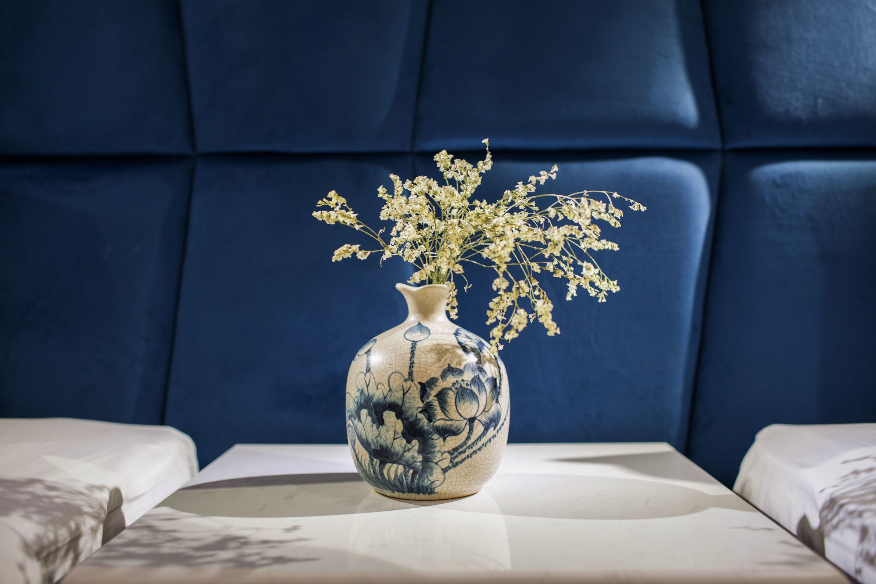 Eine Vase mit Blumen auf einem Tisch in einem Raum mit blau gepolsterten Kopfteilen.
