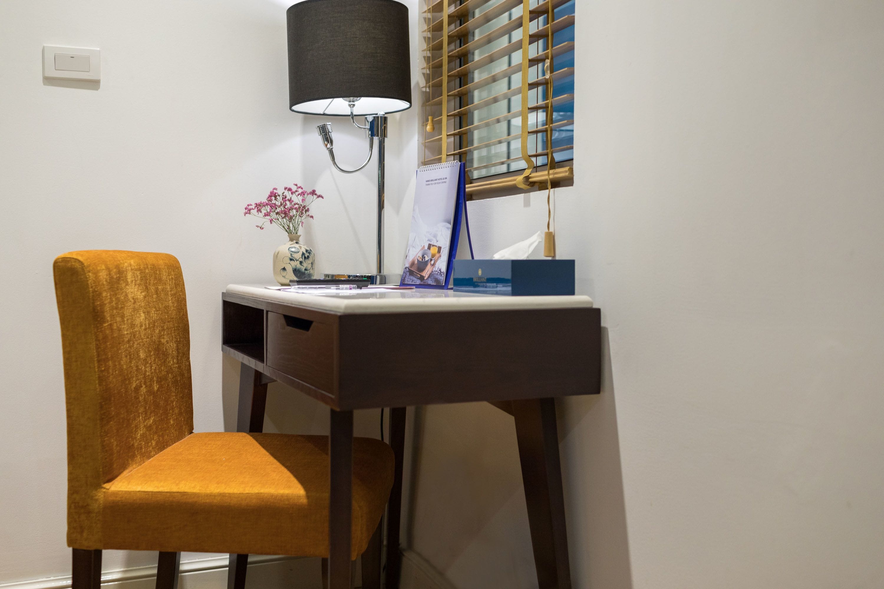 A desk with a lamp, a chair, a vase with flowers, and a calendar.