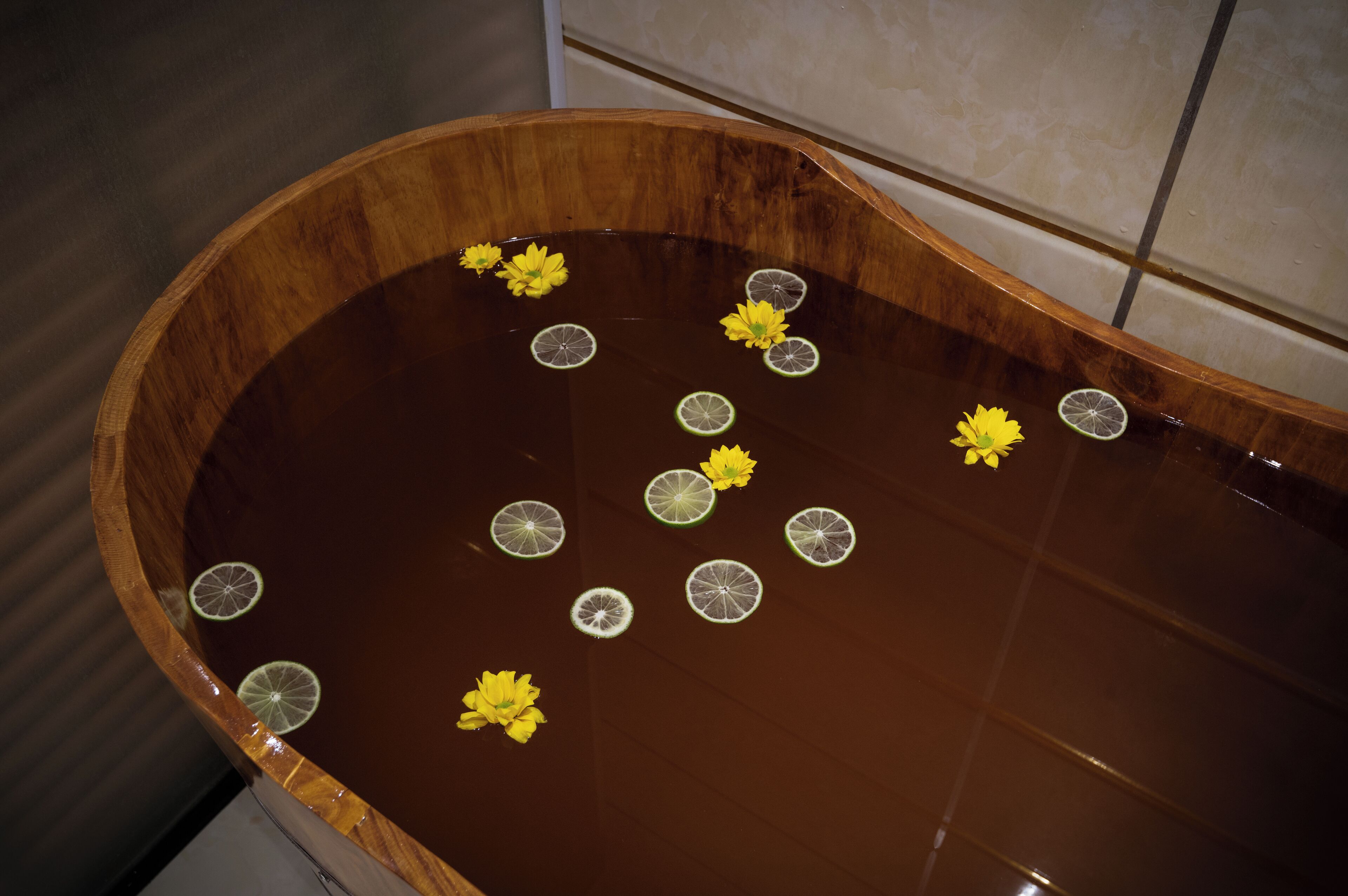 Una bañera de madera con agua, flores flotando y rodajas de lima.