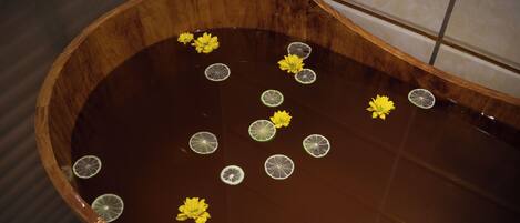 Una bañera de madera con agua, flores flotando y rodajas de lima.