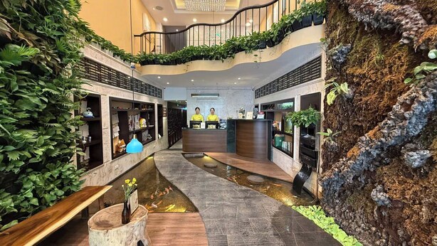 Een hotel lobby met een centraal gelegen receptiebalie, een waterpartij en weelderige beplanting.