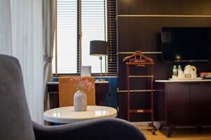 A modern hotel room with a round table, a vase with flowers, a TV, a wardrobe, and a desk with a lamp.