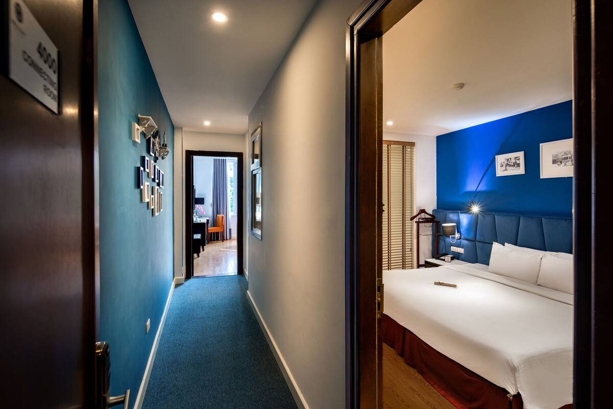 A hotel room with a blue accent wall, a large bed, a nightstand, and a wall-mounted shelf with framed pictures.