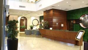 A hotel reception area with a modern design, featuring a wooden reception desk, a green accent wall, and a large circular mirror above the desk. - Gokulam Park Doha (Doha)