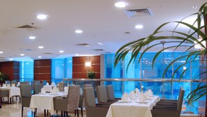 A restaurant with tables set for dining, a large window with a view, and a modern interior design. - Gokulam Park Doha (Doha)