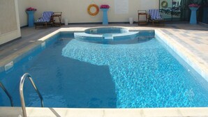 A swimming pool with a small hot tub, lounge chairs, and a lifebuoy on the wall. - Gokulam Park Doha (Doha)