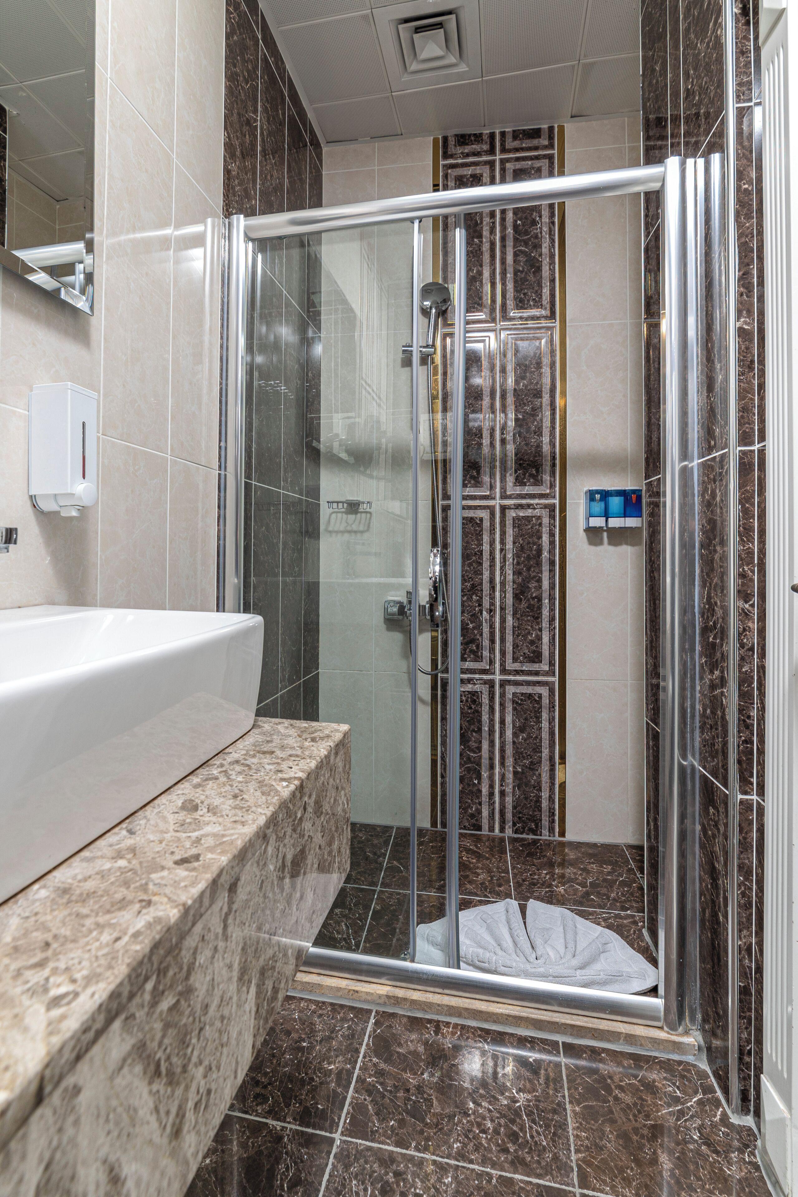 A modern bathroom with a glass-enclosed shower, a marble countertop, and a wall-mounted soap dispenser.