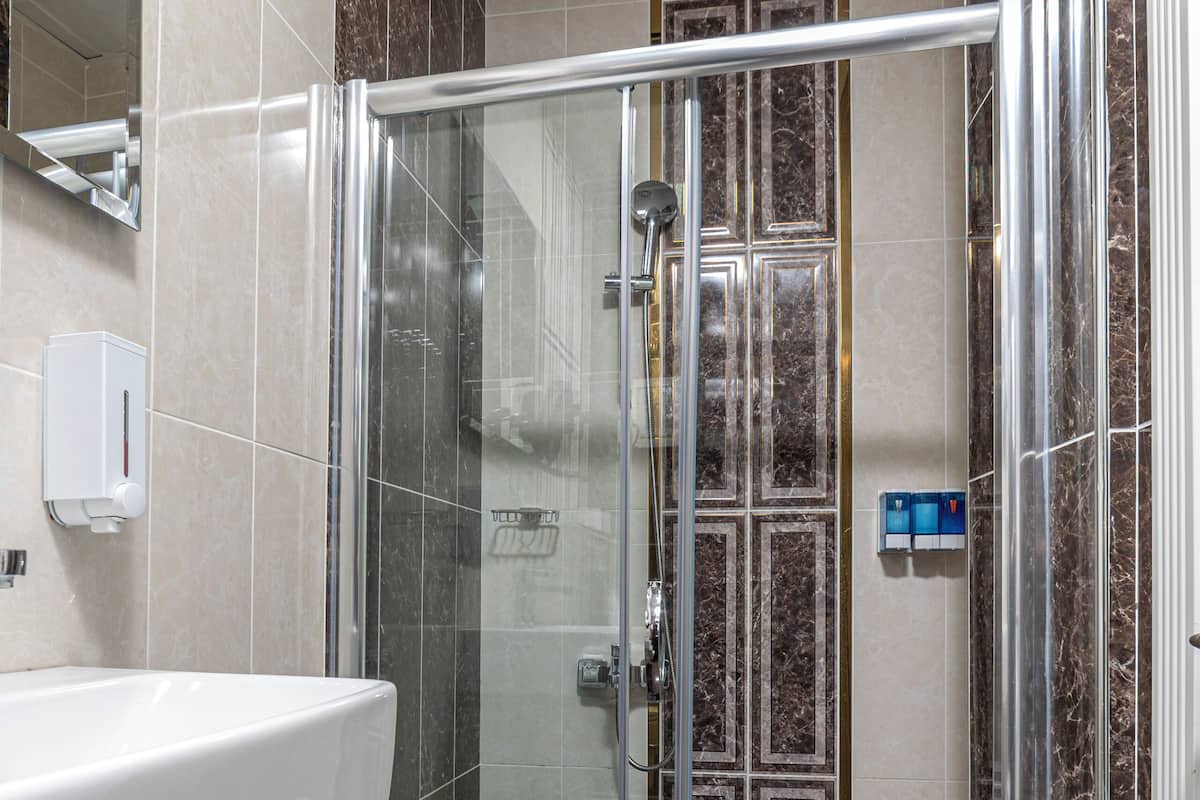 A modern bathroom with a glass-enclosed shower, a marble countertop, and a wall-mounted soap dispenser.