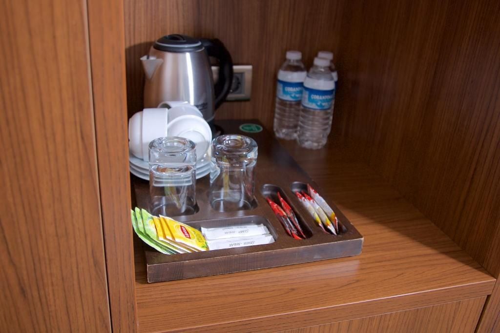 A wooden cabinet with a coffee maker, water bottles, a tray with utensils, and a small dish.