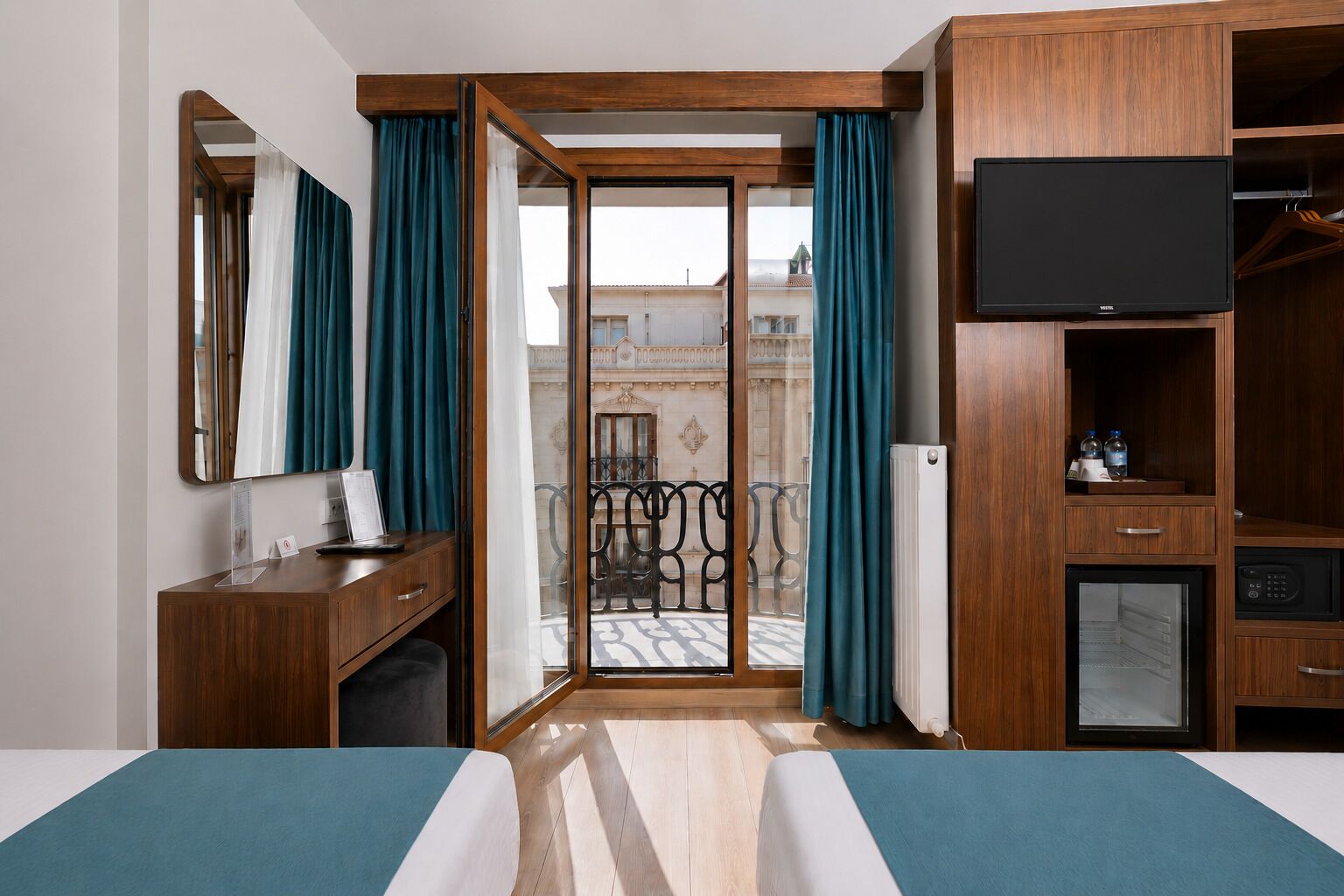 A hotel room with a bed, a desk, a television, and a sliding door leading to a balcony.