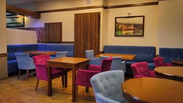 A restaurant with blue and red upholstered seating, wooden tables, and a large painting of a cityscape on the wall.