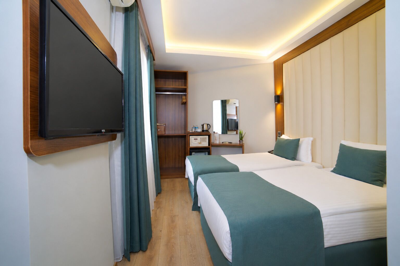 Une chambre d’hôtel avec deux lits, une télévision, un bureau avec un miroir et une armoire.