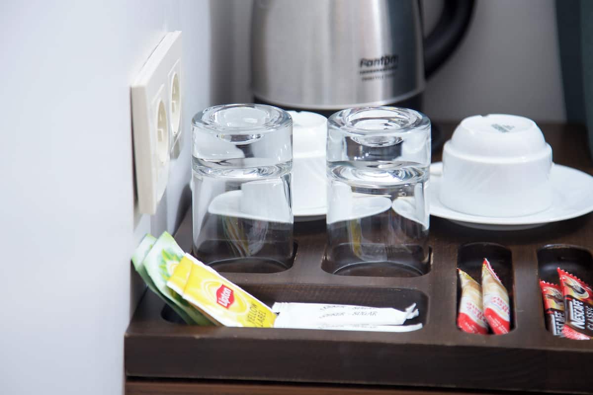 A hotel room's minibar with clear glasses, a white cup, and some snacks.