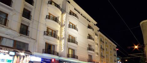 A multi-story hotel with balconies, a shop on the ground floor, and illuminated signage.