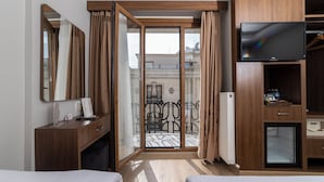 Une chambre d’hôtel équipée d’un lit, d’un bureau, d’une télévision, d’un mini-réfrigérateur et d’une porte-fenêtre coulissante donnant sur un balcon extérieur.