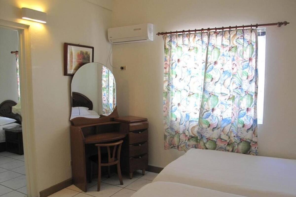 Un dormitorio con cama, un escritorio con silla, un espejo y una ventana con cortinas estampadas.