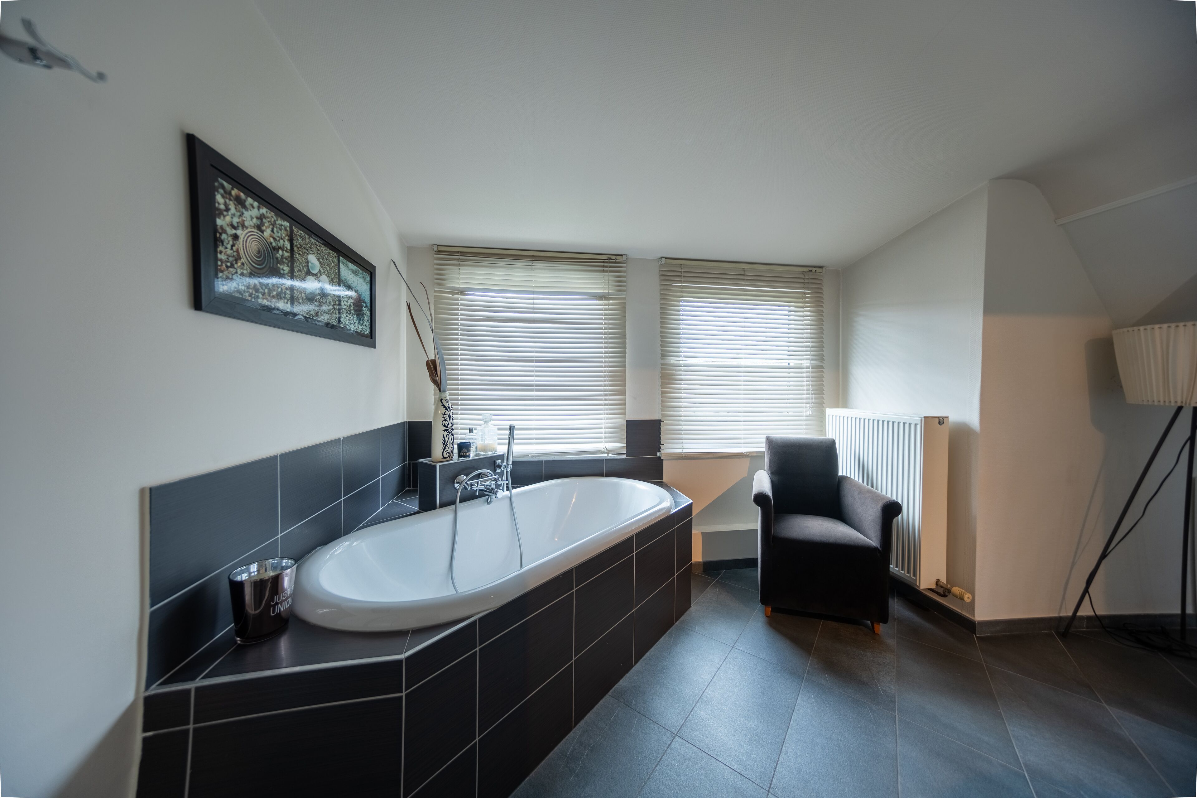 A modern bathroom with a freestanding bathtub, black tiles, a chair, and a radiator.