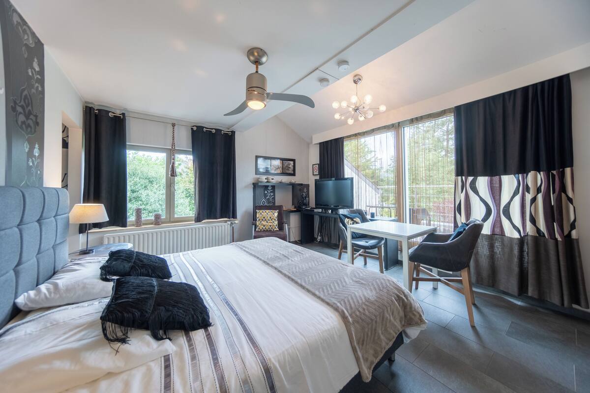 Una habitación de hotel moderna con una cama grande, un escritorio, una silla, un ventilador de techo y un televisor.