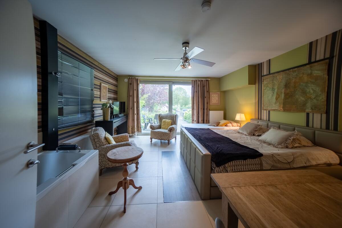 Habitación de hotel con cama, escritorio, silla, una mesita, televisión y ventana con cortinas.