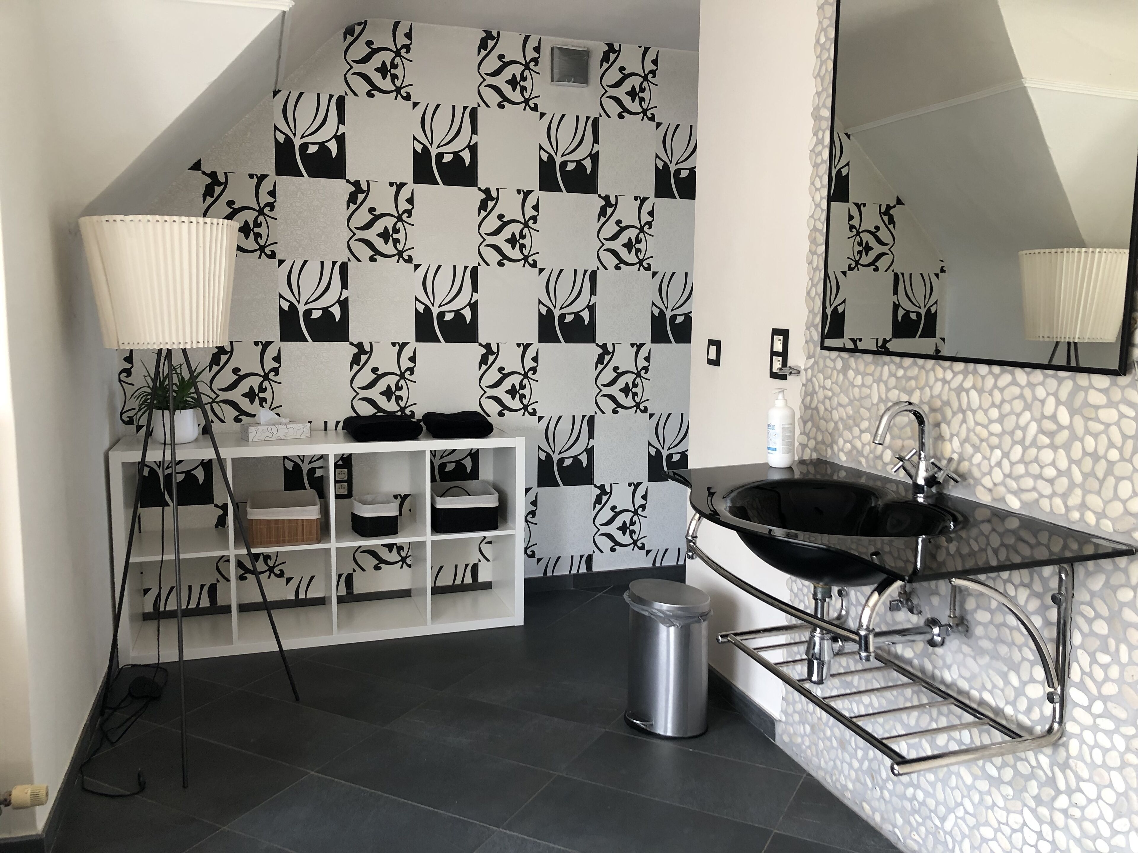 Een moderne badkamer met een zwart-wit geruite wand, een witte wastafel met opbergruimte, een zwarte wasbak en een spiegel.