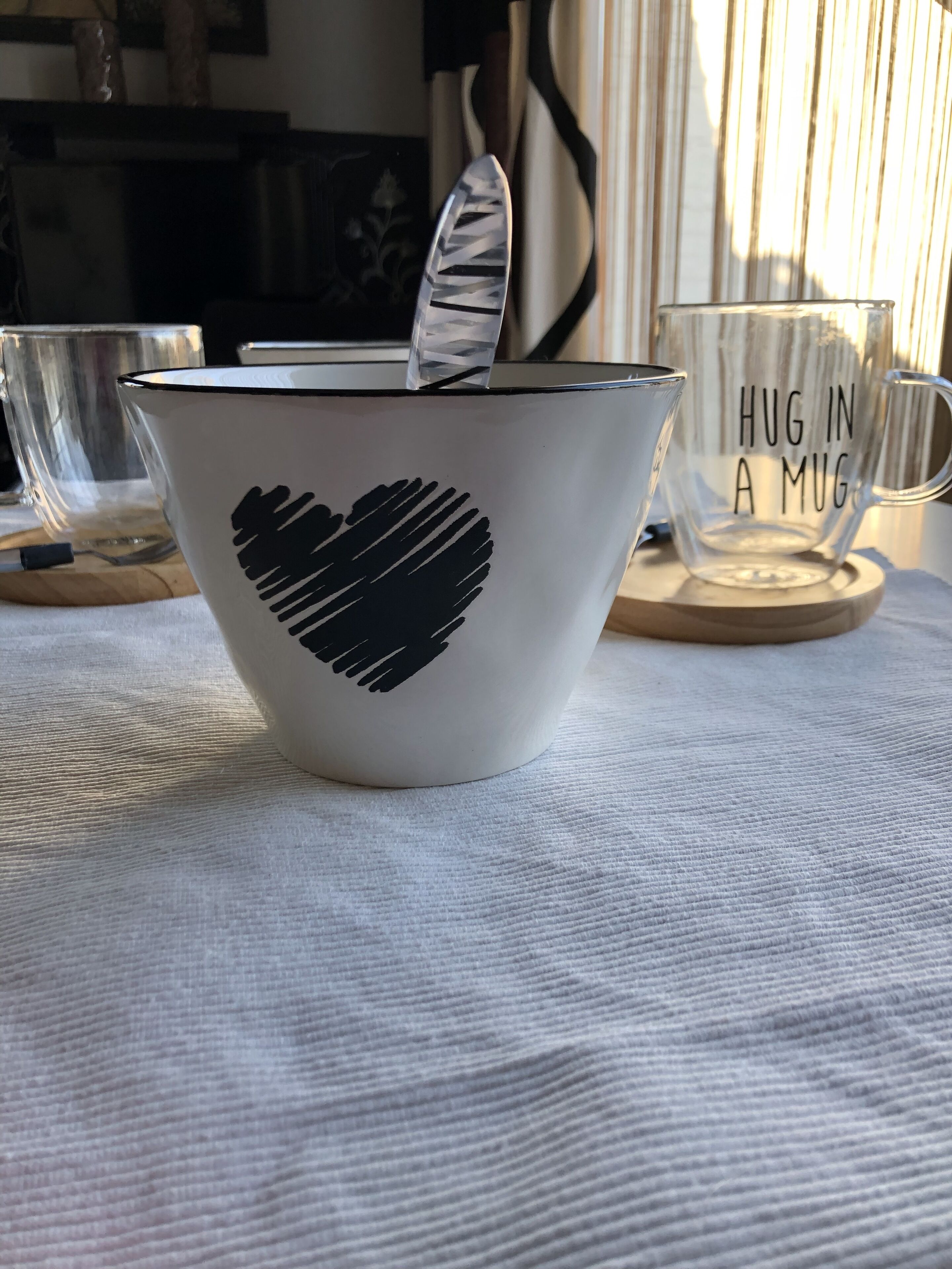 A white ceramic mug with a heart design and the text "HUG IN A MUG" on a coaster.