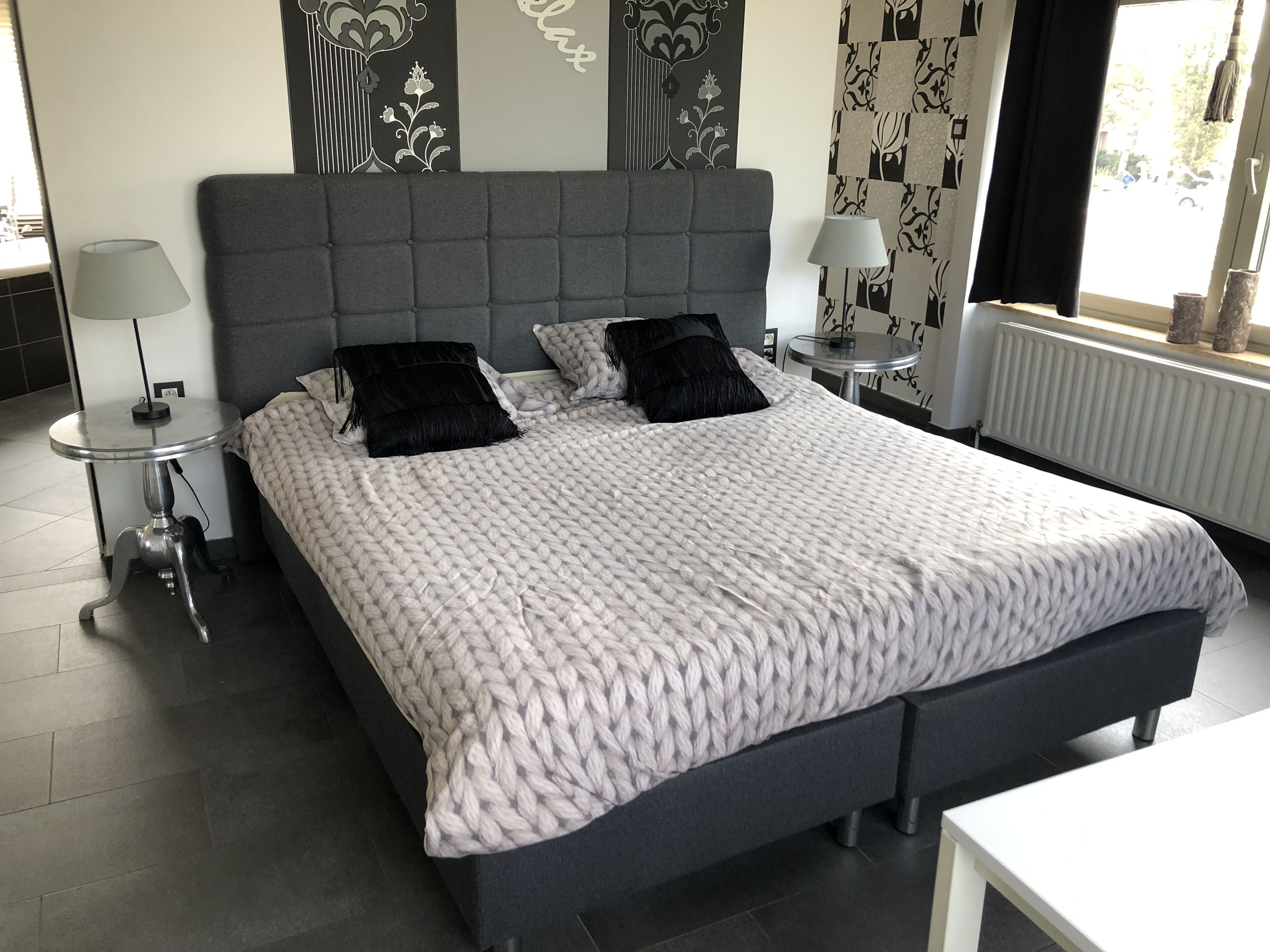 A modern bedroom with a large bed, two bedside tables, a small round table, and a radiator.