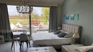 A modern bedroom with a large bed, a sofa, a dining table, and a view of the outdoors. - B&B De Witte Merel Deluxe (Beringen)
