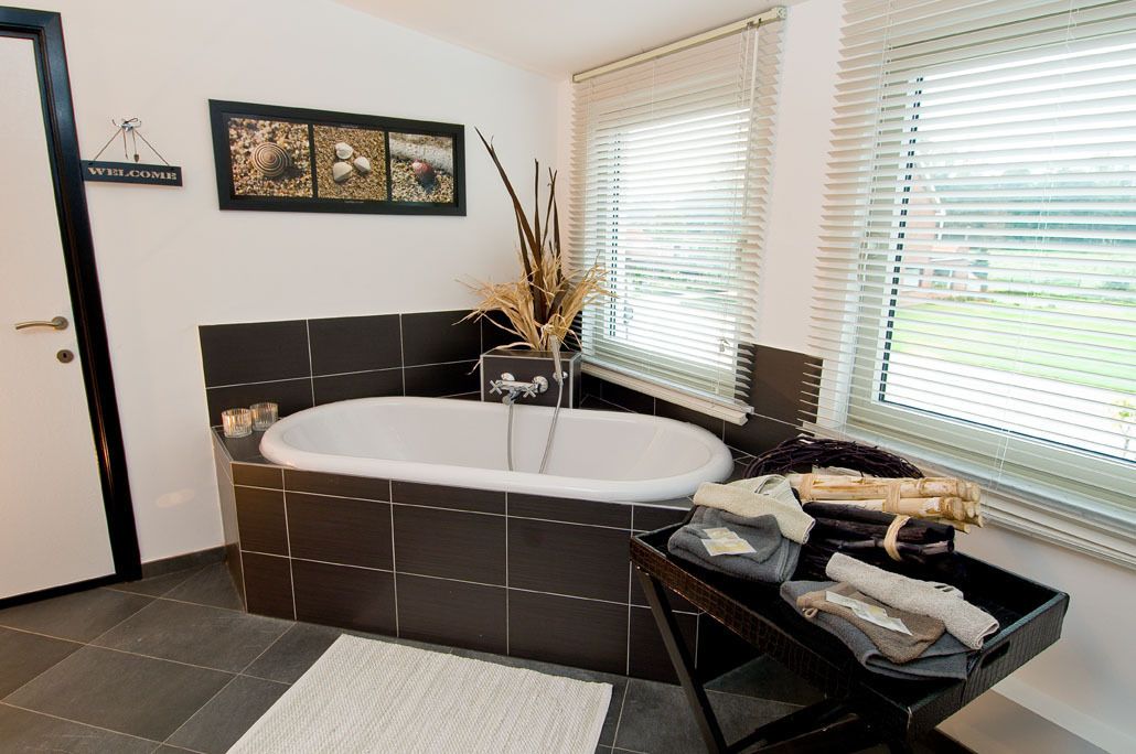 A modern bathroom with a freestanding bathtub, a welcome sign, framed artwork, and a basket of towels.