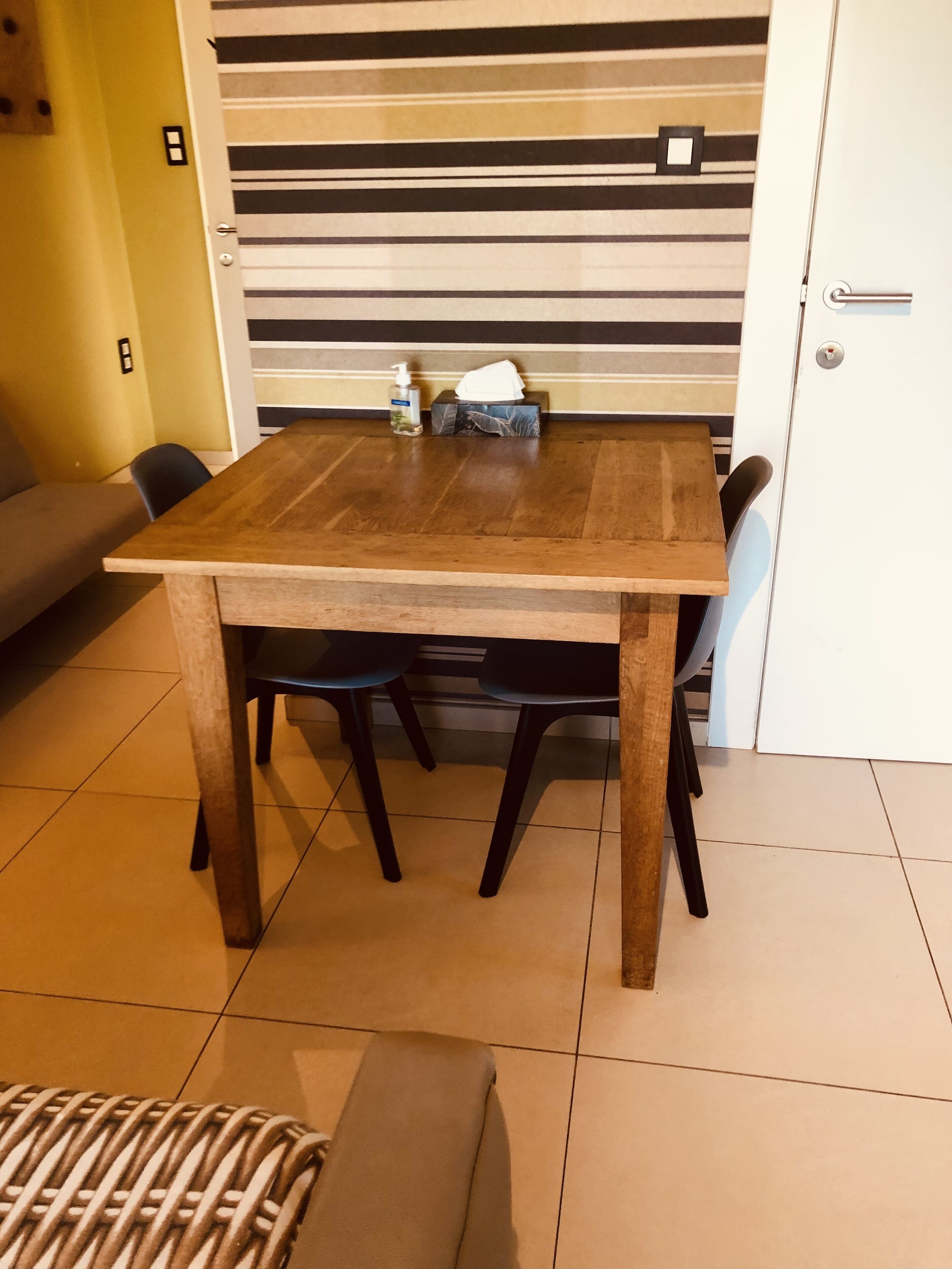 Un coin repas avec une table en bois, quatre chaises, un canapé et un mur à rayures en arrière-plan.