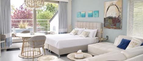 A modern bedroom with a large bed, a sofa, a dining area, and a chandelier.
